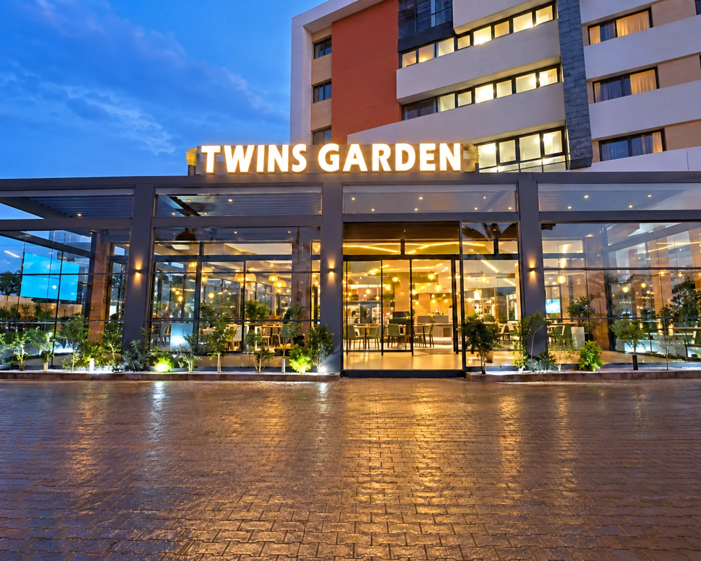 Façade du café-restaurant Twins Garden en soirée, photographie améliorée par IA